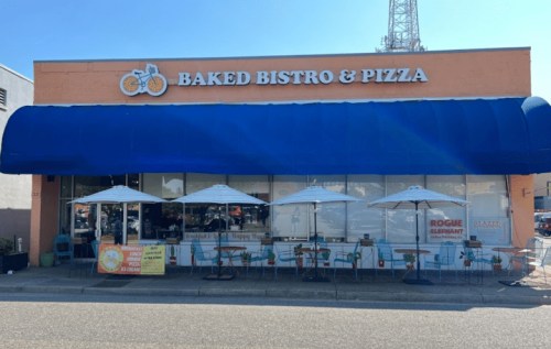 Exterior of Baked Bistro & Pizza with a blue awning, outdoor seating, and umbrellas on a sunny day.