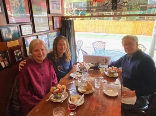 A group of three people enjoying a meal at a restaurant, with plates of food and drinks on the table.