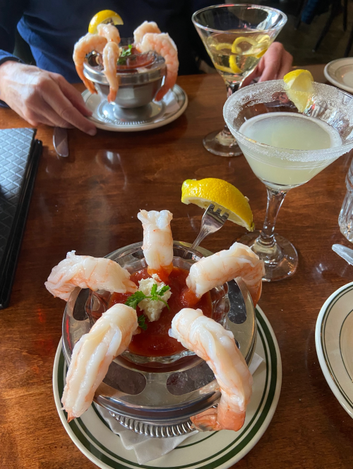 Two shrimp cocktails with shrimp arranged around a bowl of cocktail sauce, accompanied by martinis on a wooden table.
