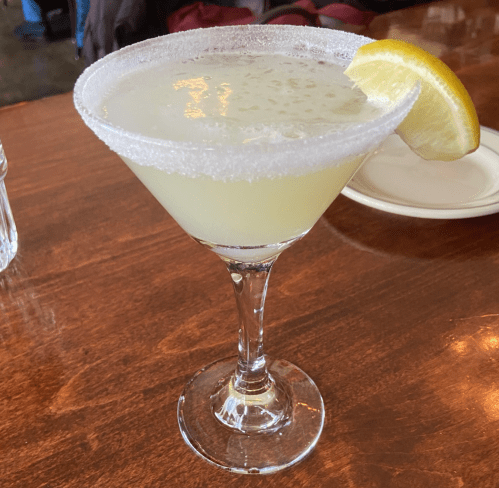 A refreshing margarita in a salt-rimmed glass, garnished with a lemon wedge, on a wooden table.