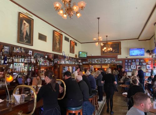 A busy bar with patrons seated at the counter, vintage decor, and multiple TVs displaying sports.