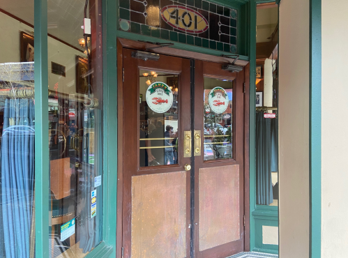 Entrance to a shop with wooden double doors, featuring decorative glass and signage on the windows.