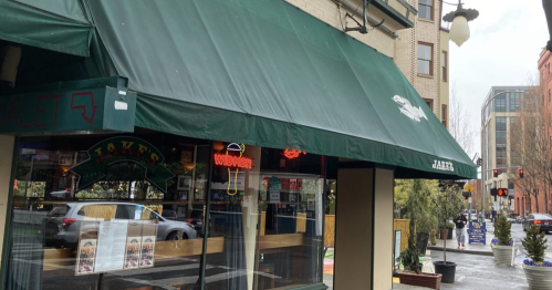 Exterior of Jake's restaurant with a green awning, street view, and nearby buildings on a rainy day.