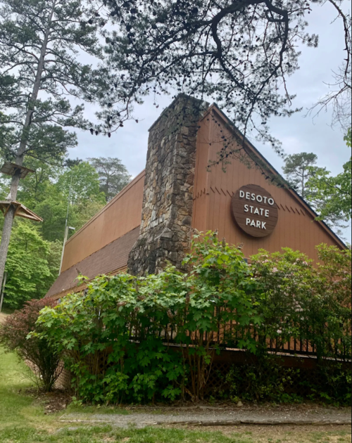 A rustic building at Desoto State Park, surrounded by greenery and tall trees under a cloudy sky.