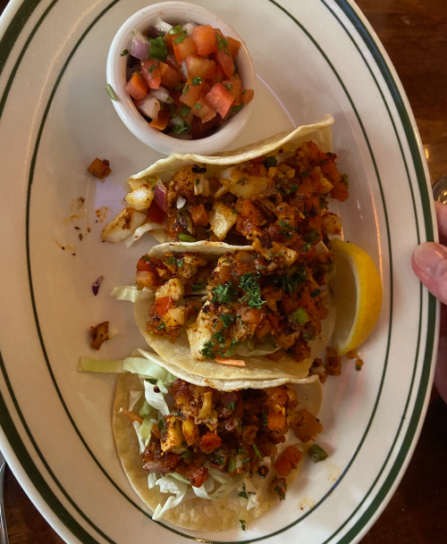Three tacos filled with seasoned vegetables and shrimp, served with a side of pico de gallo and a lemon wedge.