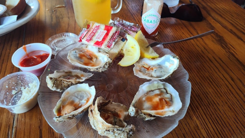 A plate of oysters on the half shell with lemon, hot sauce, and cocktail sauce, set on a wooden table.