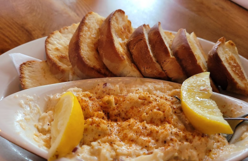 A dish of creamy seafood dip garnished with lemon slices, served with toasted bread slices on the side.