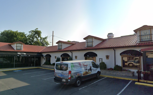 A restaurant with a red-tiled roof and a delivery van parked in front, under a clear blue sky.