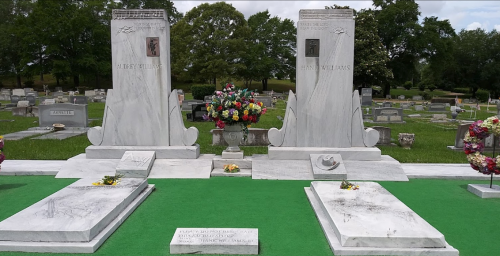 Two marble gravestones in a cemetery, surrounded by flowers and greenery, honoring Alton and Henry Williams.
