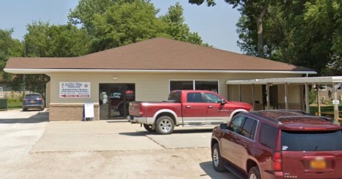 A one-story building with a brown roof, featuring a sign that says "Open," surrounded by parked cars.