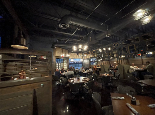 A dimly lit restaurant interior with wooden decor, tables filled with diners, and decorative mirrors on the walls.