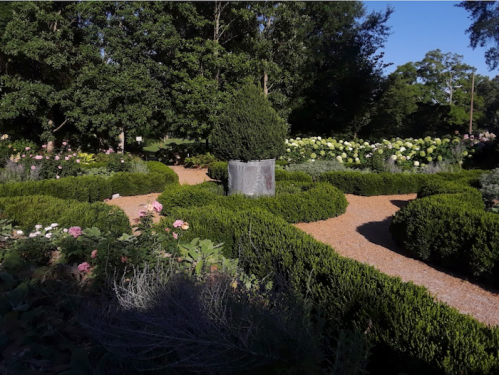 A serene garden with winding paths, lush greenery, and blooming flowers under a clear blue sky.