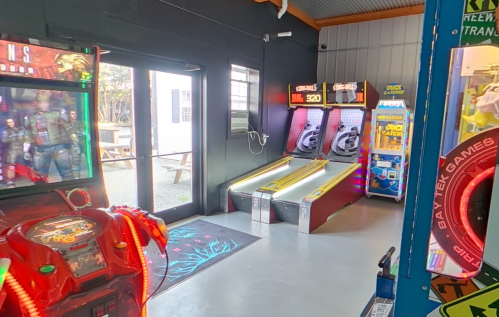 A bright arcade room featuring two ski ball machines and a video game cabinet near an open door.