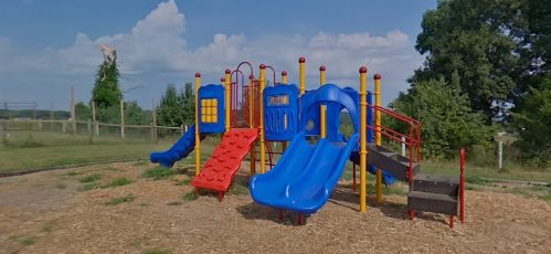 Colorful playground equipment with slides and climbing structures, set in a grassy area under a blue sky.