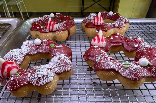Four festive donuts with red icing, sprinkles, and decorative toppings, arranged on a cooling rack.