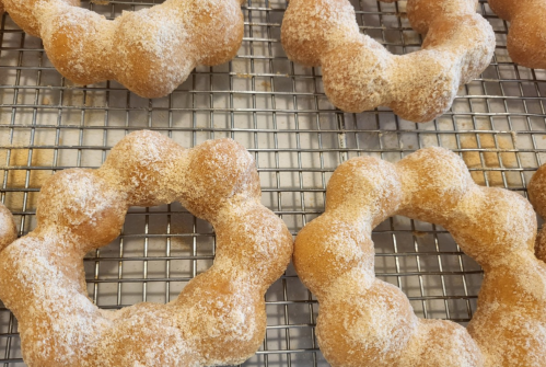 Freshly baked, sugar-coated doughnuts shaped like rings, resting on a wire cooling rack.