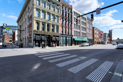 Street view of a city intersection featuring buildings, crosswalks, and traffic lights under a partly cloudy sky.