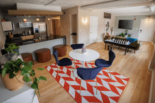 A modern living space featuring a kitchen, dining table with blue chairs, and a cozy seating area with a TV.