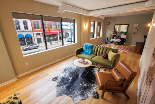 A modern living room with a green sofa, coffee table, and large windows overlooking a city street.