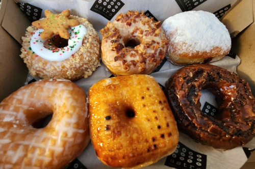 A box of assorted donuts, including glazed, chocolate, and festive varieties with toppings and decorations.