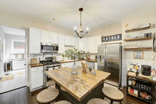 A modern kitchen with white cabinets, a wooden island, and a dining table, featuring stainless steel appliances and decor.