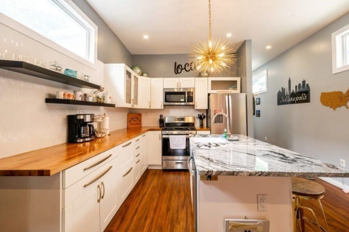 Modern kitchen with white cabinets, stainless steel appliances, a wooden countertop, and stylish lighting fixtures.