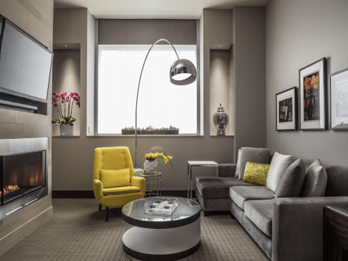 Modern living room featuring a gray sofa, yellow armchair, coffee table, and a large window with plants.
