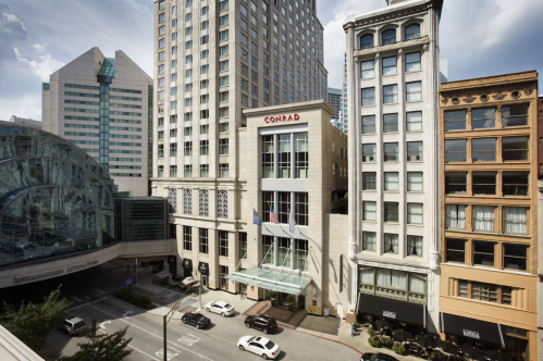 View of the Conrad hotel surrounded by modern and historic buildings under a partly cloudy sky.
