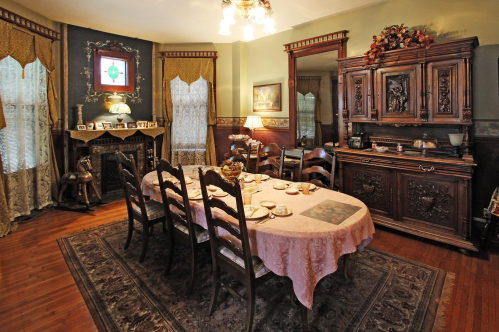 A vintage dining room with a large table set for a meal, ornate furniture, and elegant curtains.