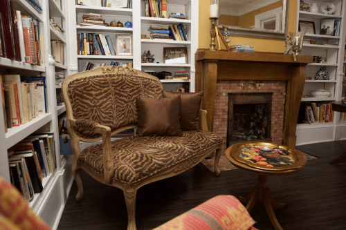 Cozy reading nook with a patterned loveseat, a small table, and a fireplace surrounded by bookshelves.