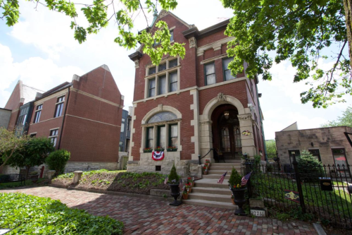 Historic brick building with ornate architecture, surrounded by greenery and a brick pathway.