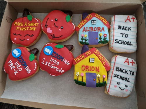 A box of colorful back-to-school themed cookies, including apples and schoolhouse designs with cheerful messages.