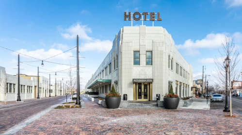 Art Deco hotel building with a prominent sign, surrounded by a brick-paved street and decorative planters.