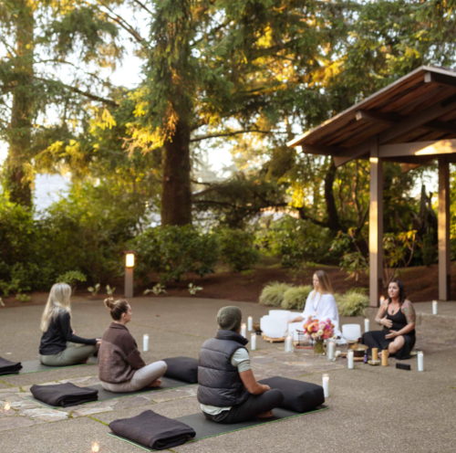 A serene outdoor setting with people meditating on mats, surrounded by nature and soft candlelight.
