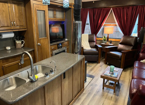 Cozy living space with a kitchen island, leather chairs, and warm wood accents, featuring red curtains and modern decor.