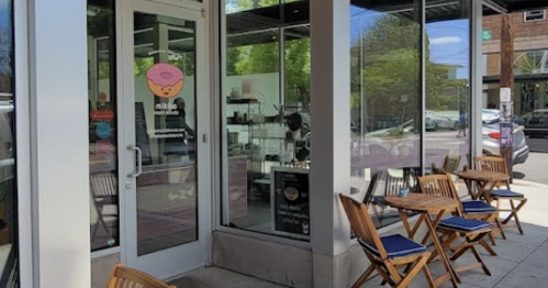 Exterior of a café with a pink sign, outdoor seating, and large windows on a sunny day.