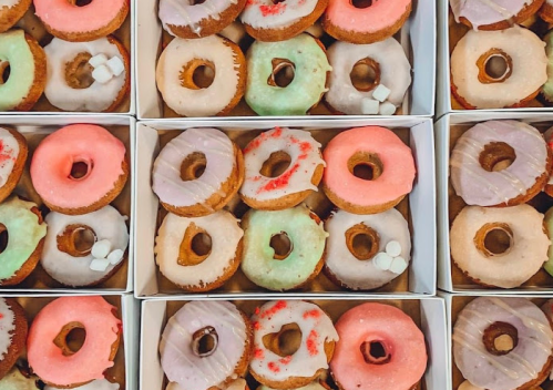 A variety of colorful donuts in boxes, featuring pink, green, and lavender icing with sprinkles and marshmallows.