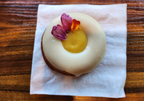A round dessert with a white icing, topped with a yellow filling and edible flowers, resting on a napkin.