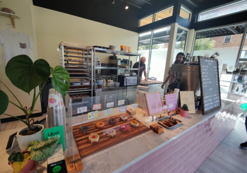A cozy café interior with a display of colorful donuts, a coffee machine, and staff preparing orders in the background.