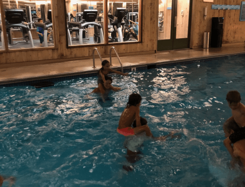 A group of children play in a swimming pool, splashing water and enjoying themselves in a lively atmosphere.