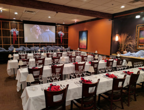 A dining room set for a formal event, featuring tables with white tablecloths, red napkins, and a large screen in the background.