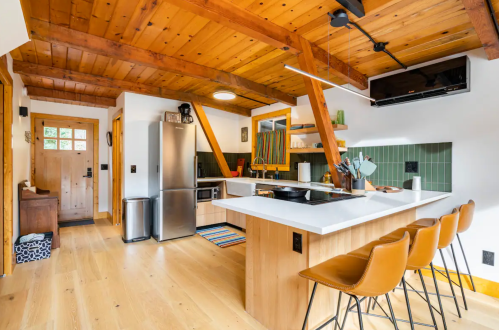 Modern kitchen with wooden beams, green tiles, stainless steel appliances, and a breakfast bar with three stools.