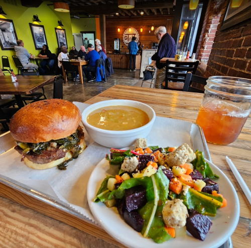A hearty meal featuring a burger, soup, and salad on a wooden table in a cozy restaurant setting.