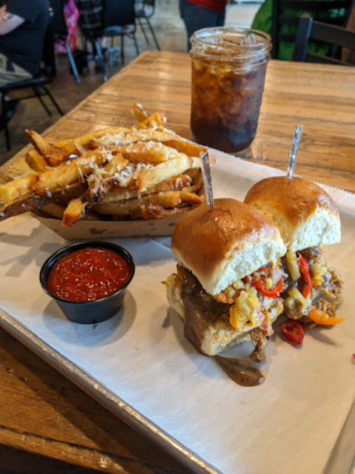 Two sliders with pulled pork and toppings, served with a side of loaded fries and a glass of iced tea.