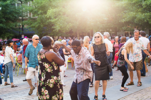 A lively outdoor scene with people dancing and enjoying a sunny day in a crowded plaza.