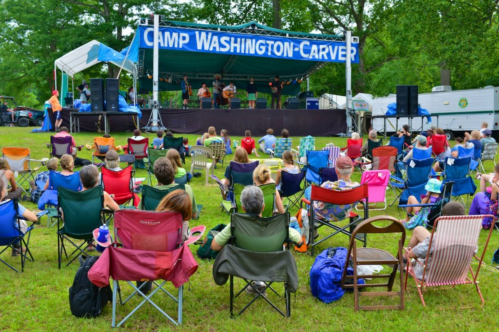 Audience seated in folding chairs at Camp Washington-Carver, enjoying a live performance on stage.