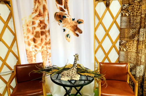 A cozy seating area with two chairs, a table, and giraffe-themed decor, including a backdrop and a plush giraffe.