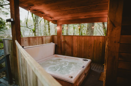 A cozy wooden hot tub area surrounded by trees, with soft lighting and a serene atmosphere.