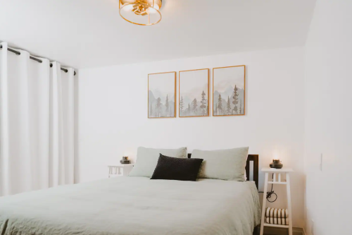 A cozy bedroom featuring a bed with light bedding, two nightstands, and framed mountain artwork on the wall.