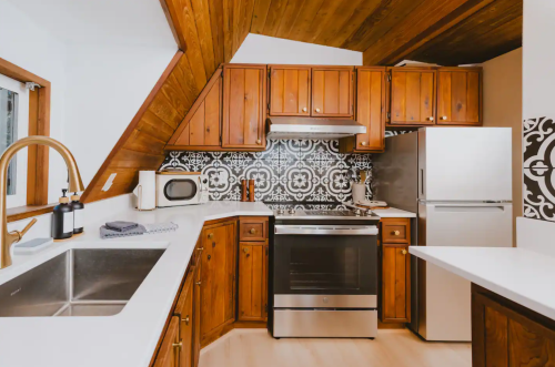 A modern kitchen with wooden cabinets, stainless steel appliances, and patterned backsplash under a sloped ceiling.